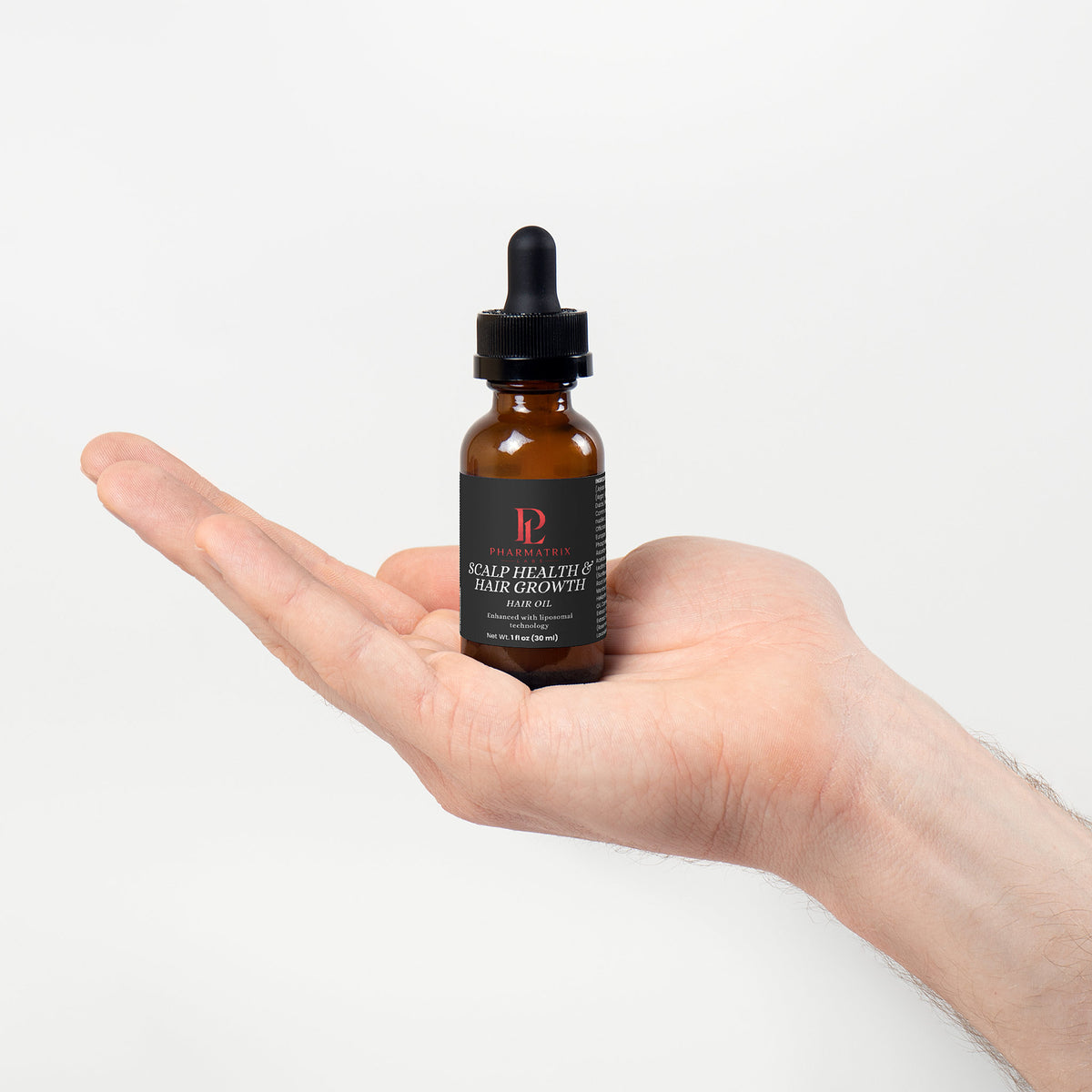 Hand holding a bottle of Vitamin hair serum with a dropper on a white background