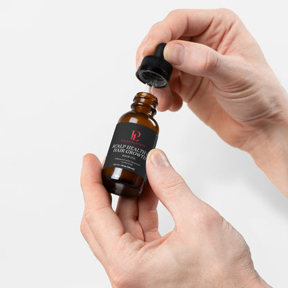 Hand holding a bottle of  hair serum with a dropper against a white background
